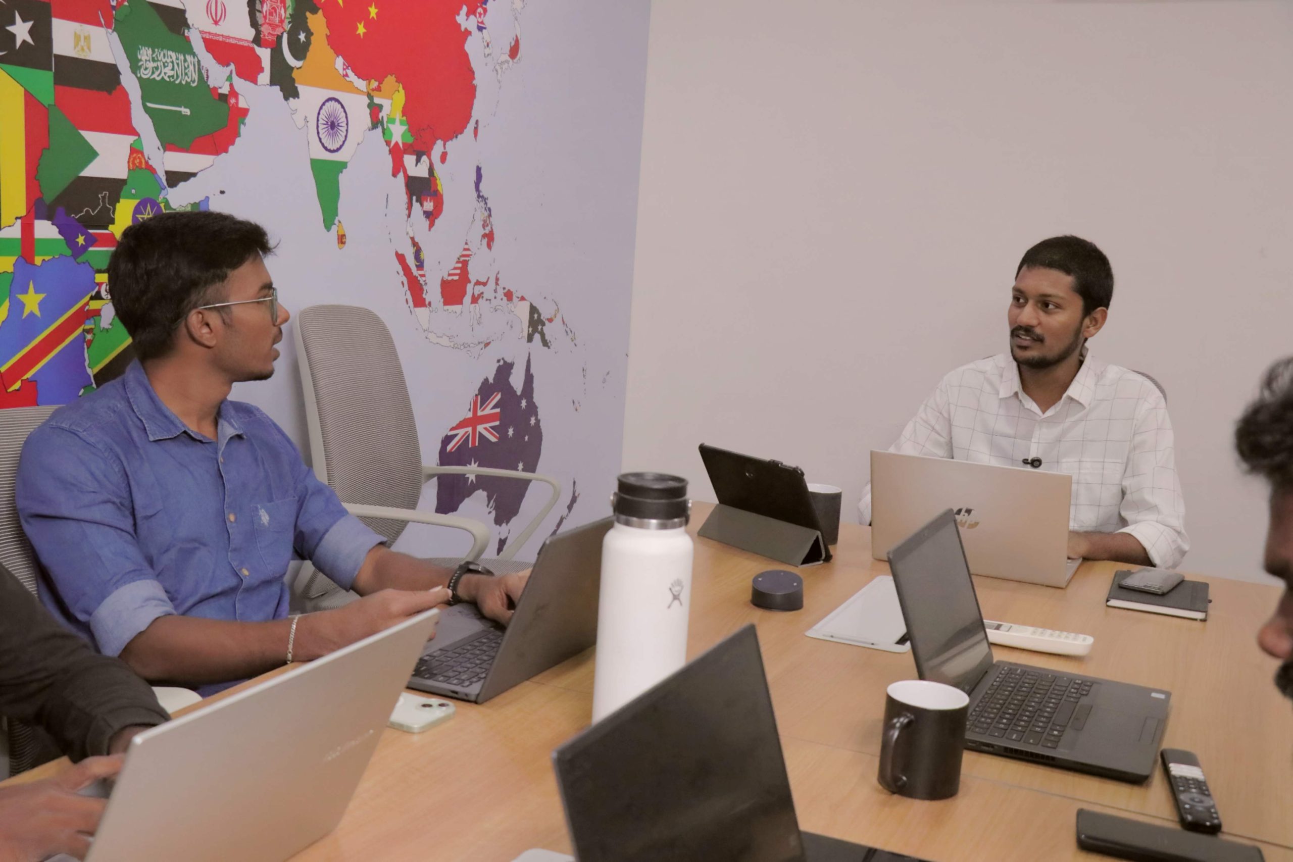 Siteligent team collaborating on laptops in office with world map background.