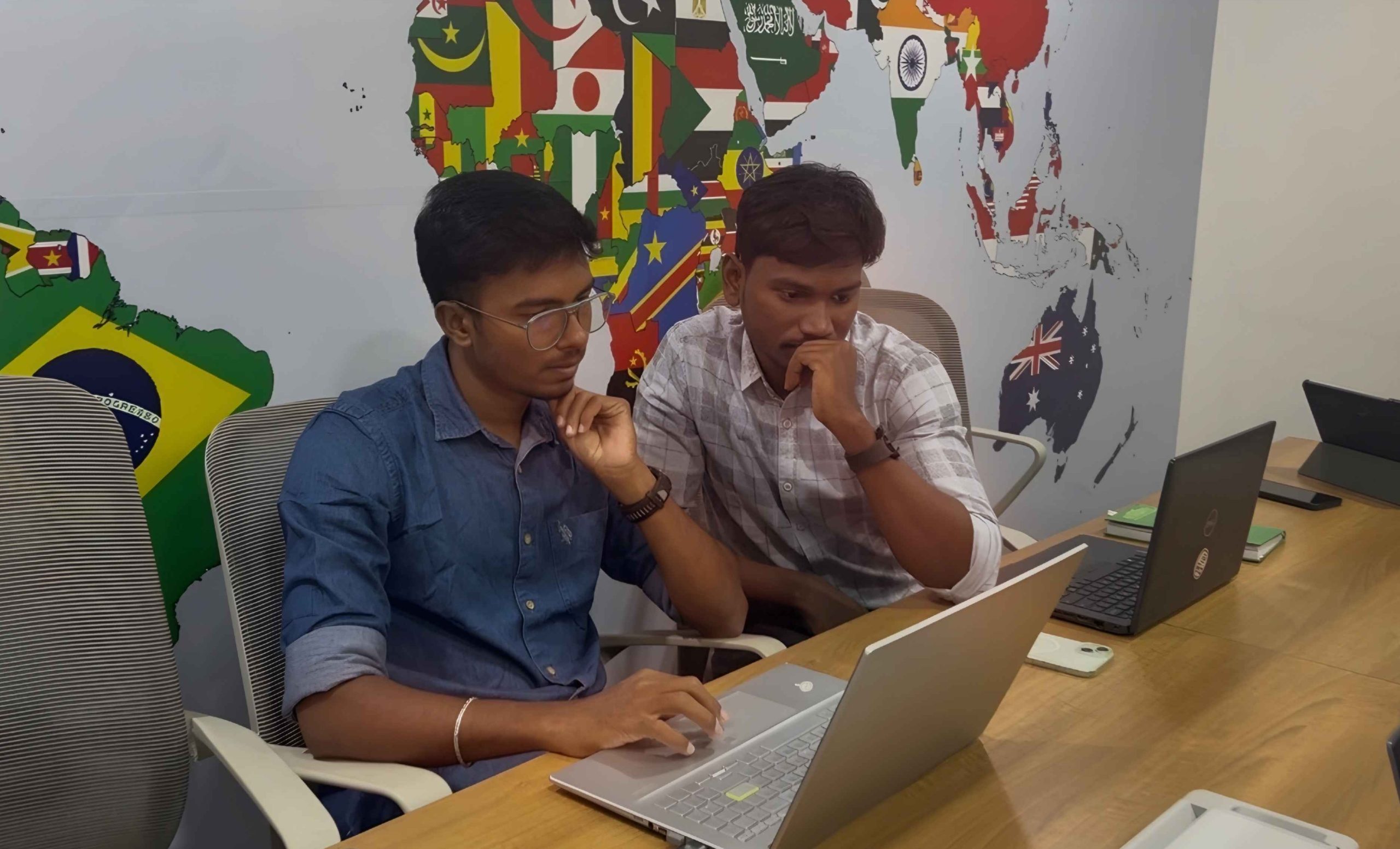 Siteligent team members collaborating on laptops in office with world map background.